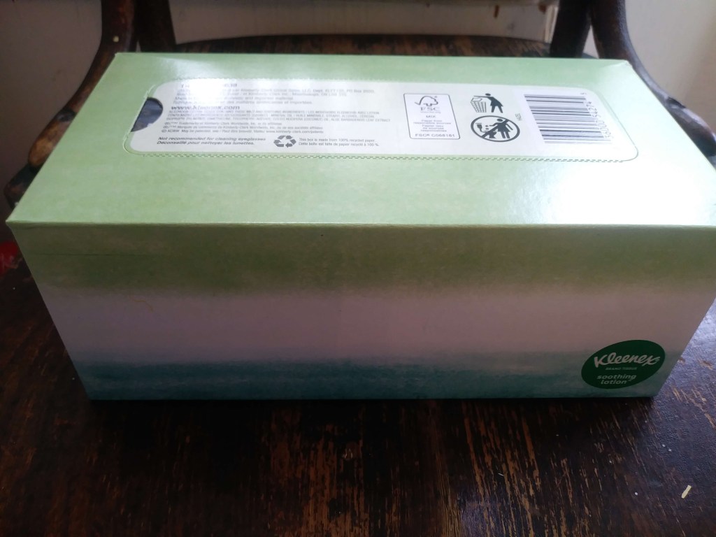 The long side and upper part of the tissue box. Rectangular, white, green, and blue pastel design. Green and white logo on the right hand hand lower corner. 